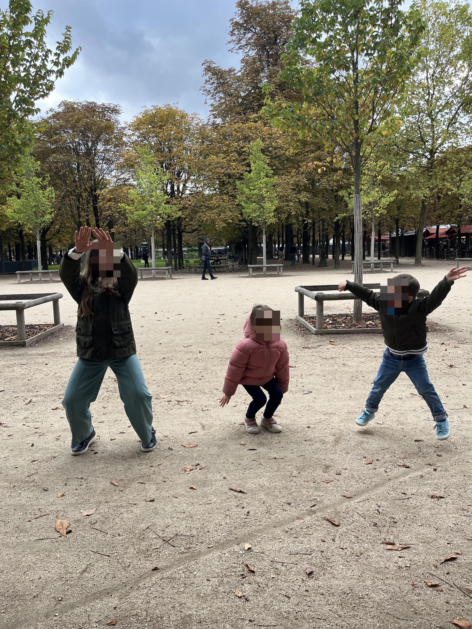 Three children doing jumping jacks on a gravel path in the Tuileries Garden