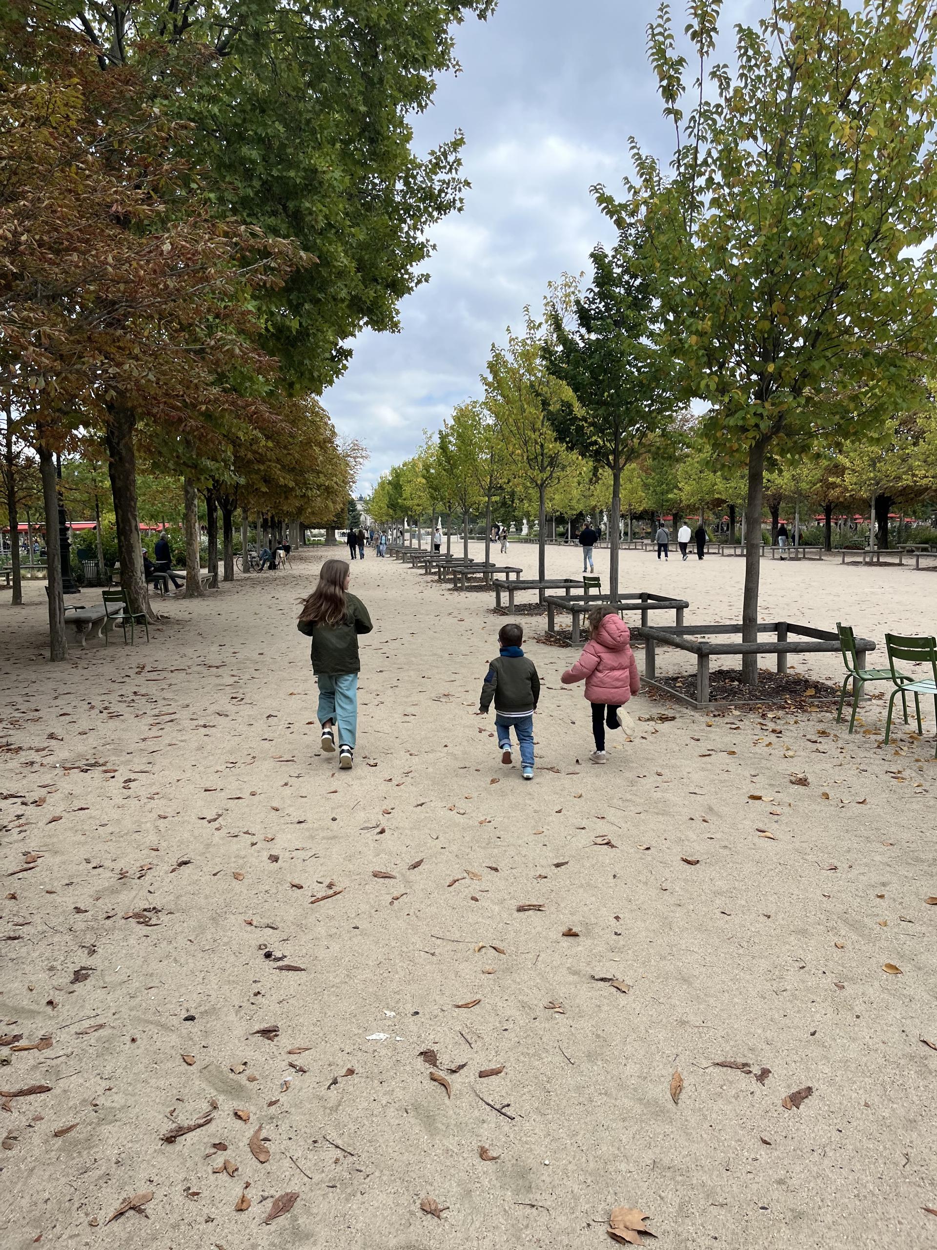 Three children running down a tree-lined path in the Tuileries Garden